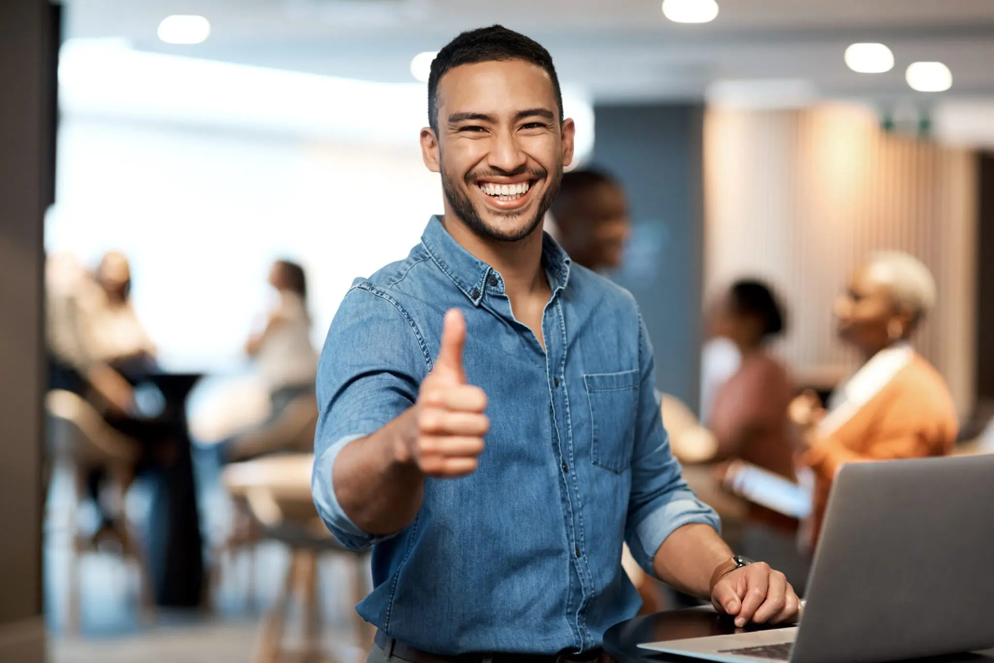 Smiling man giving a thumbs-up in a casual office setting.