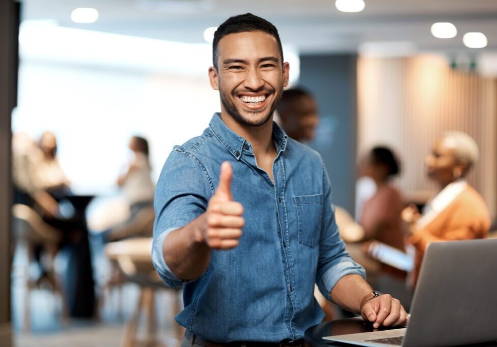 Smiling man giving a thumbs-up in a casual office setting.